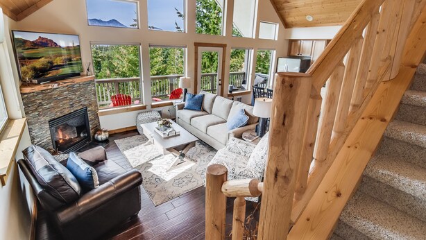 A spacious living area with a fireplace, a sofa, and a coffee table. There are multiple windows providing views of the outdoors. - 1PM In/Out + Pool Access | Scenic Mountain Cabin Built for More Family Time (Ronald)