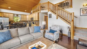 A spacious living area with a wooden staircase, a sofa, a patterned armchair, and a coffee table. - 1PM In/Out + Pool Access | Scenic Mountain Cabin Built for More Family Time (Ronald)