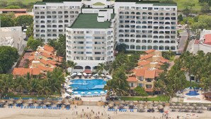 Ein Resort mit mehreren Gebäuden, einem großen Schwimmbad und einem Strandbereich mit Sonnenschirmen und Liegestühlen.