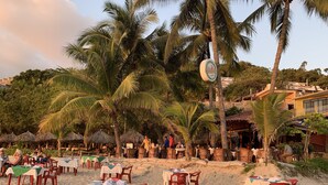 Ein Restaurant am Strand mit Außenbereich, Palmen und Meerblick.