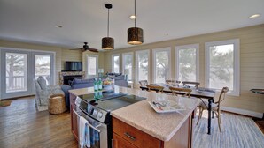 A spacious kitchen with a central island, a dining area with wooden chairs, and large windows providing views of the outdoors. - Relax, Refresh, Renew..Waterfront Cottage..Near Williamsburg (Gloucester)