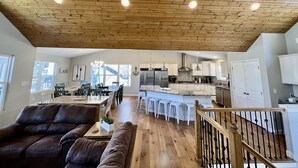 Un salón amplio con techo de madera, una mesa de comedor y una cocina con electrodomésticos de acero inoxidable.