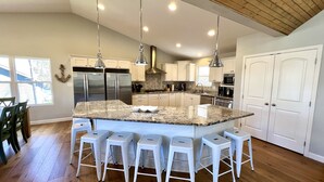 Una cocina moderna con una isla grande, taburetes de bar blancos, electrodomésticos de acero inoxidable e iluminación colgante.
