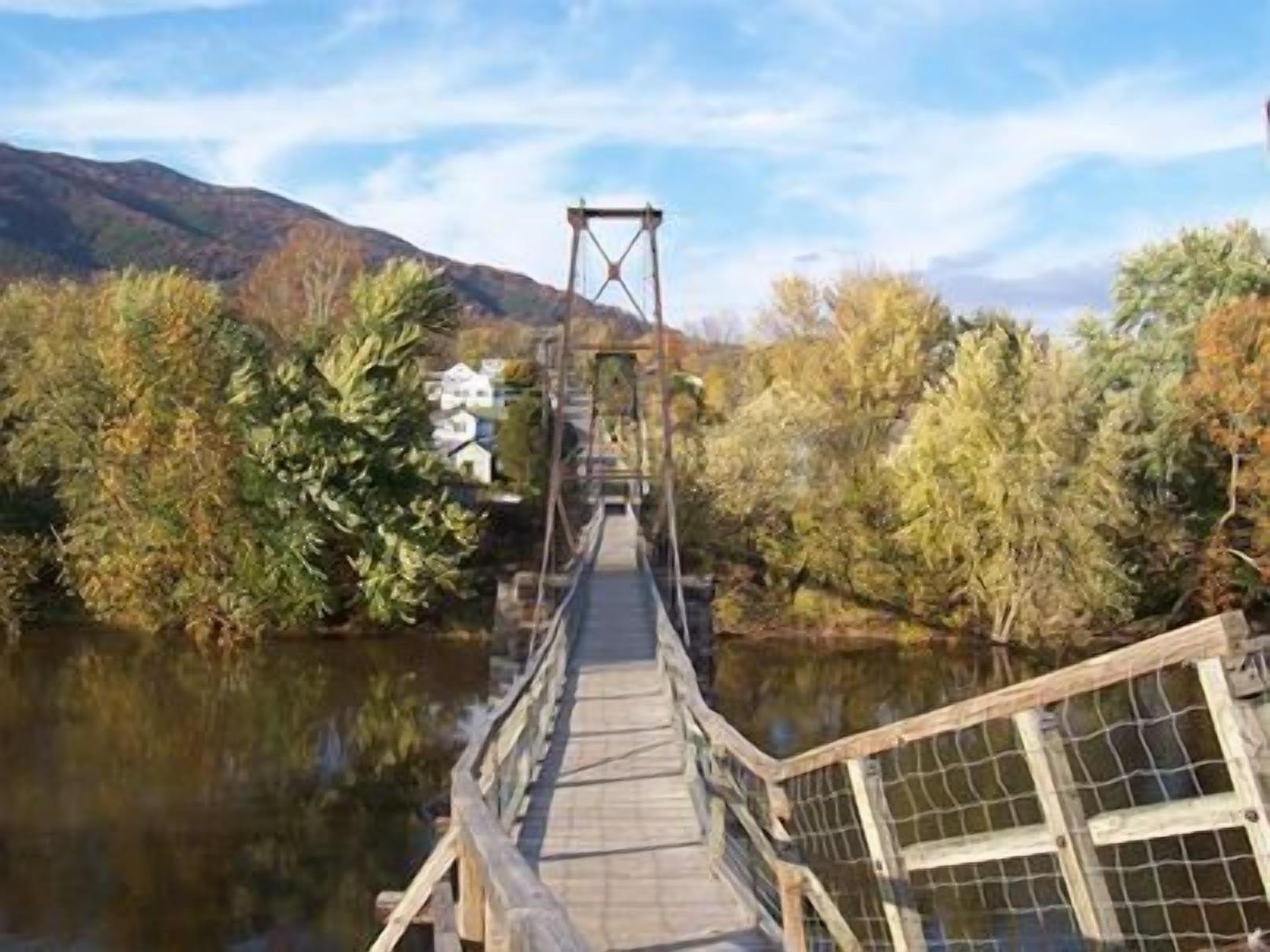 A wooden suspension bridge over a river with dense foliage on both sides.
