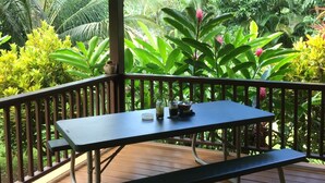 Uma área de estar coberta ao ar livre, com mesa e bancos, cercada por vegetação tropical exuberante.