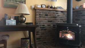 Un cuarto acogedor con chimenea de ladrillo, una mesa con lámpara, libros y una taza.