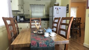 Un comedor con una mesa de madera, sillas, un mantel decorado, un hervidor y tazas.