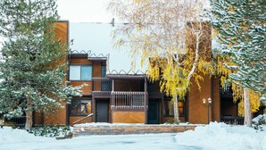 A modern two-story building with a wooden facade, a balcony with a railing, and a snow-covered ground. - Deluxe Condo -complimentary shuttle to ski- Best location, comfort & style (Park City)