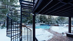 A spiral staircase leading to a covered outdoor area with a pool, surrounded by snow-covered ground and trees. - Deluxe Condo -complimentary shuttle to ski- Best location, comfort & style (Park City)