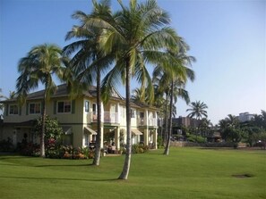 Stunning two-story house with a balcony and front porch, set amidst a beautifully manicured lawn and palm trees.