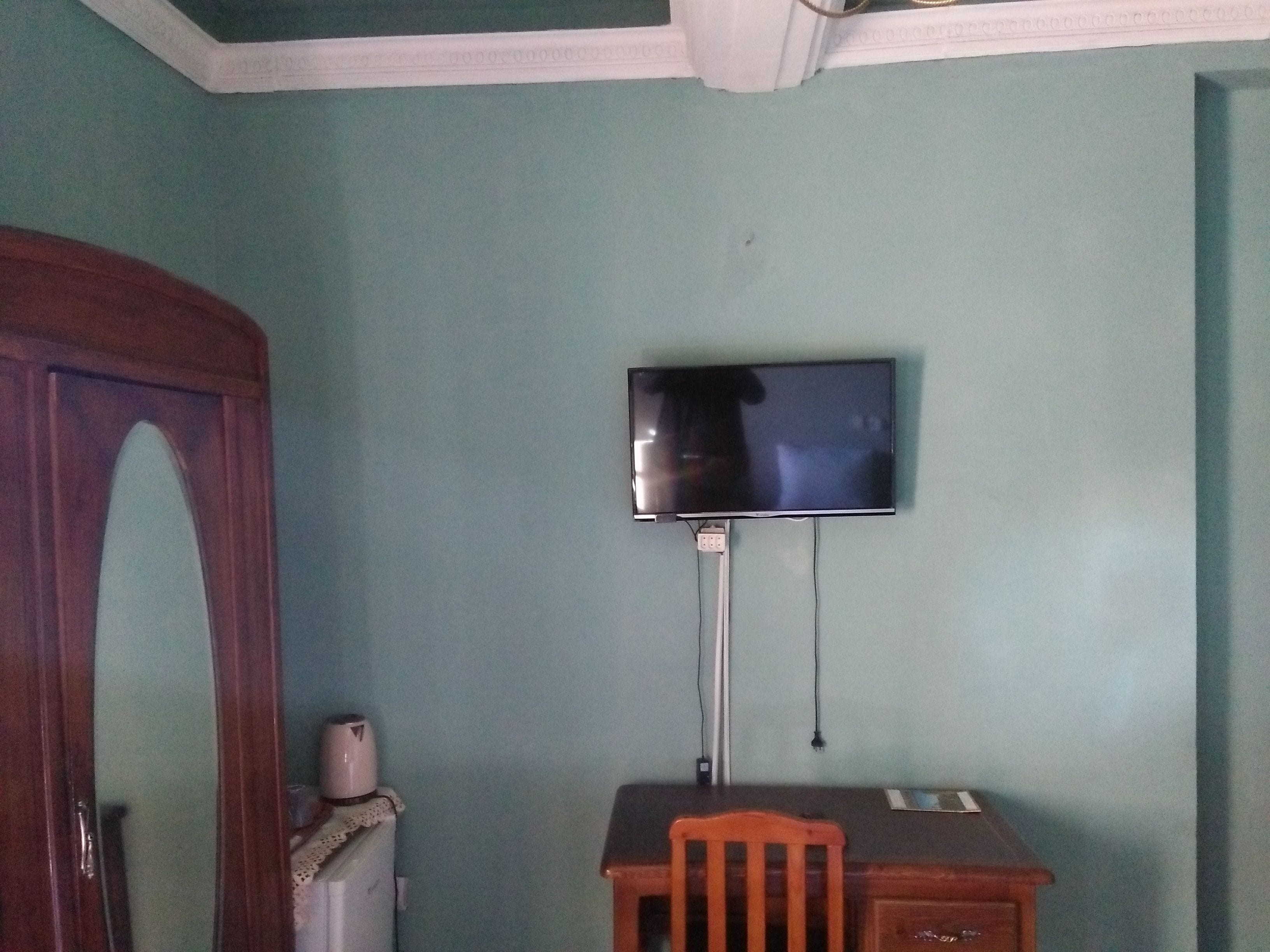 A room with teal walls, a wooden door, a desk with a chair, and a mounted television.