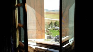 Una ventana con vistas a un paisaje rural, que incluye campos y una colina distante.
