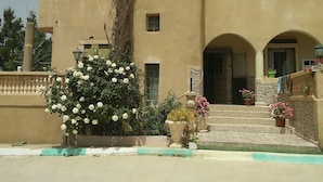 Un edificio con fachada color beige, varias ventanas y una entrada central con escalones.