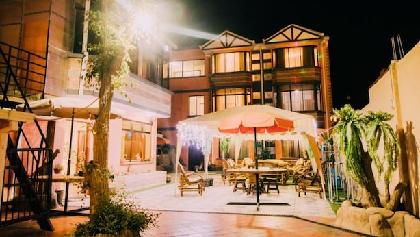 Un espace extérieur aménagé en terrasse, avec des tables et des chaises, un coin salon abrité et un bâtiment doté de nombreuses fenêtres et de balcons.