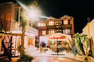 An outdoor patio area with tables and chairs, a covered seating area, and a building with multiple windows and balconies.