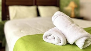 Un lit bien fait, avec du linge de lit blanc et un plaid vert, une tête de lit en bois et une lampe sur une table de chevet.