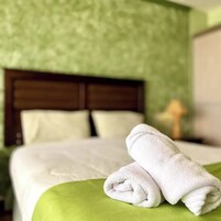 A neatly made bed with white linens and a green throw blanket, a wooden headboard, and a lamp on a bedside table.