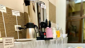 Un buffet proposant une variété d’aliments, notamment des fruits, du pain et une machine à café.