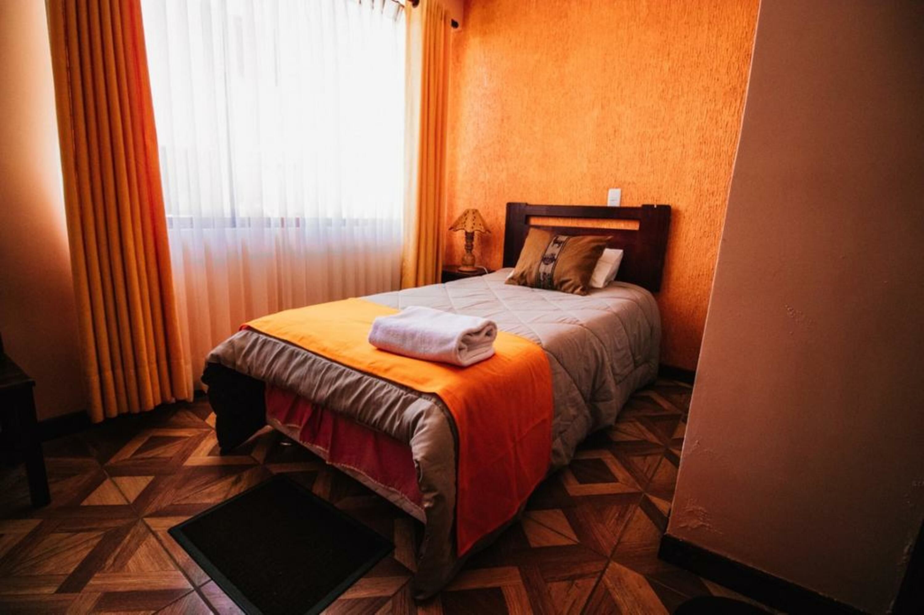 Une chambre d’hôtel avec un lit, une table de chevet, une lampe et une fenêtre avec des rideaux.