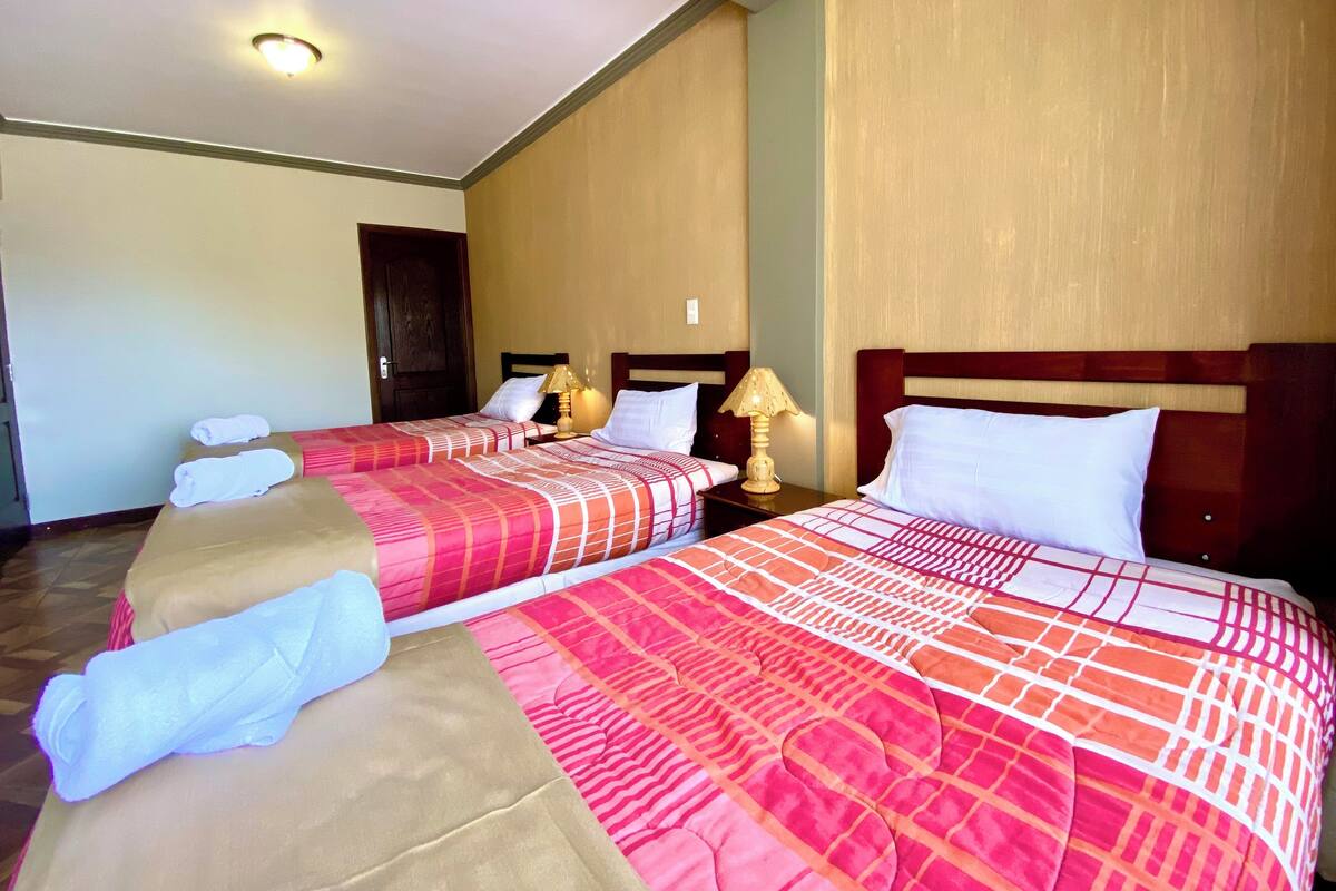 A hotel room with two beds, each with a red and white patterned bedspread, a wooden headboard, and a nightstand with a lamp.
