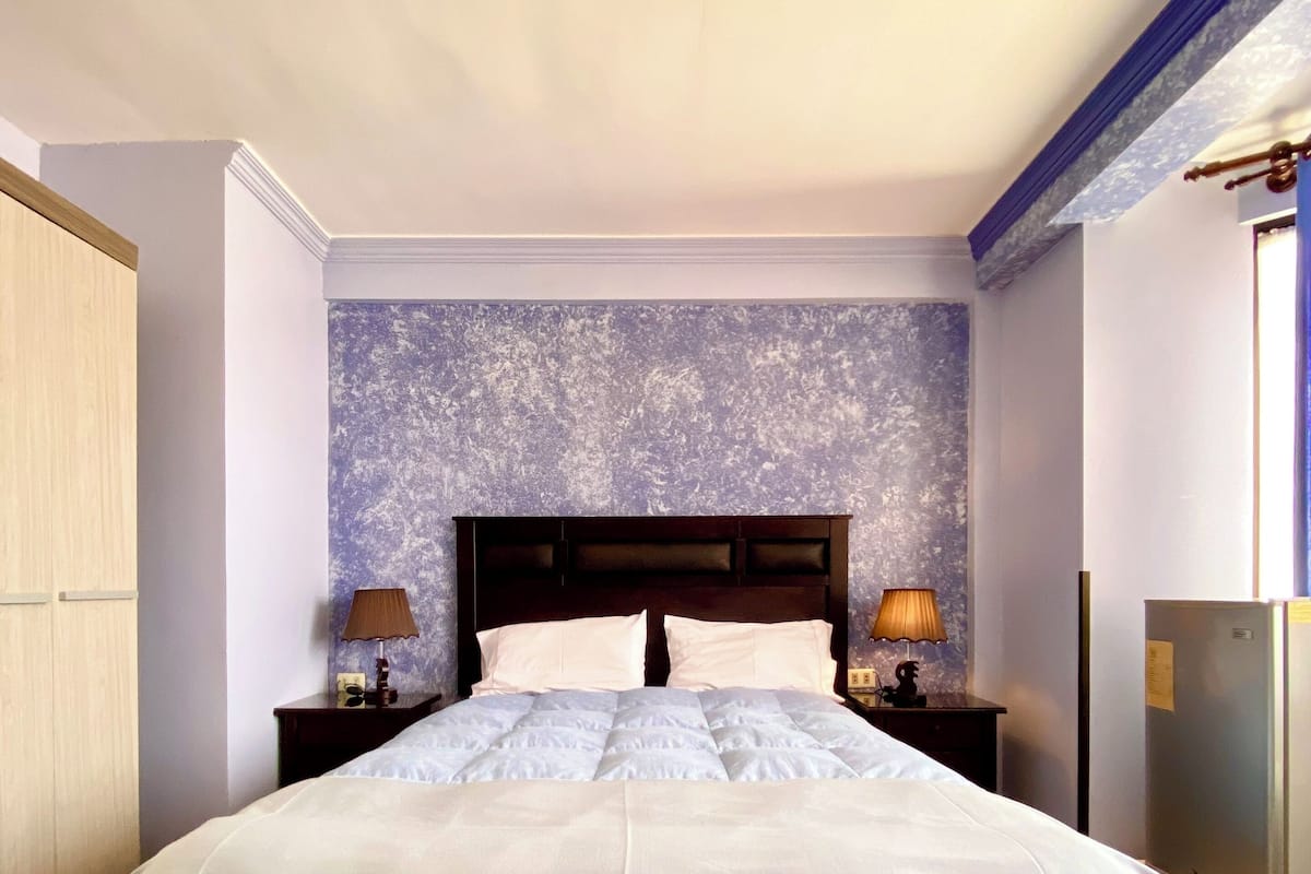 A neatly made bed with a patterned skirt, a headboard, and two bedside lamps.
