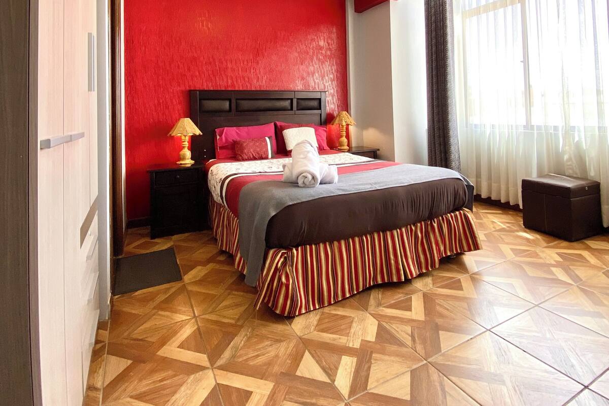 A hotel room with a bed, a nightstand, a lamp, and a window with curtains.