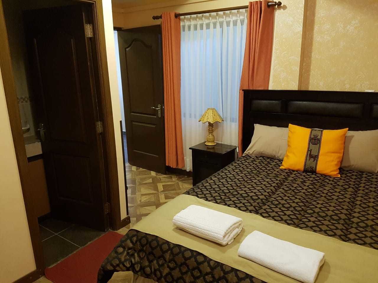 Une chambre d’hôtel avec un lit, une table de chevet, une lampe et une porte.
