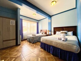 A hotel room with two beds, a wardrobe, a window with curtains, and a tiled floor.
