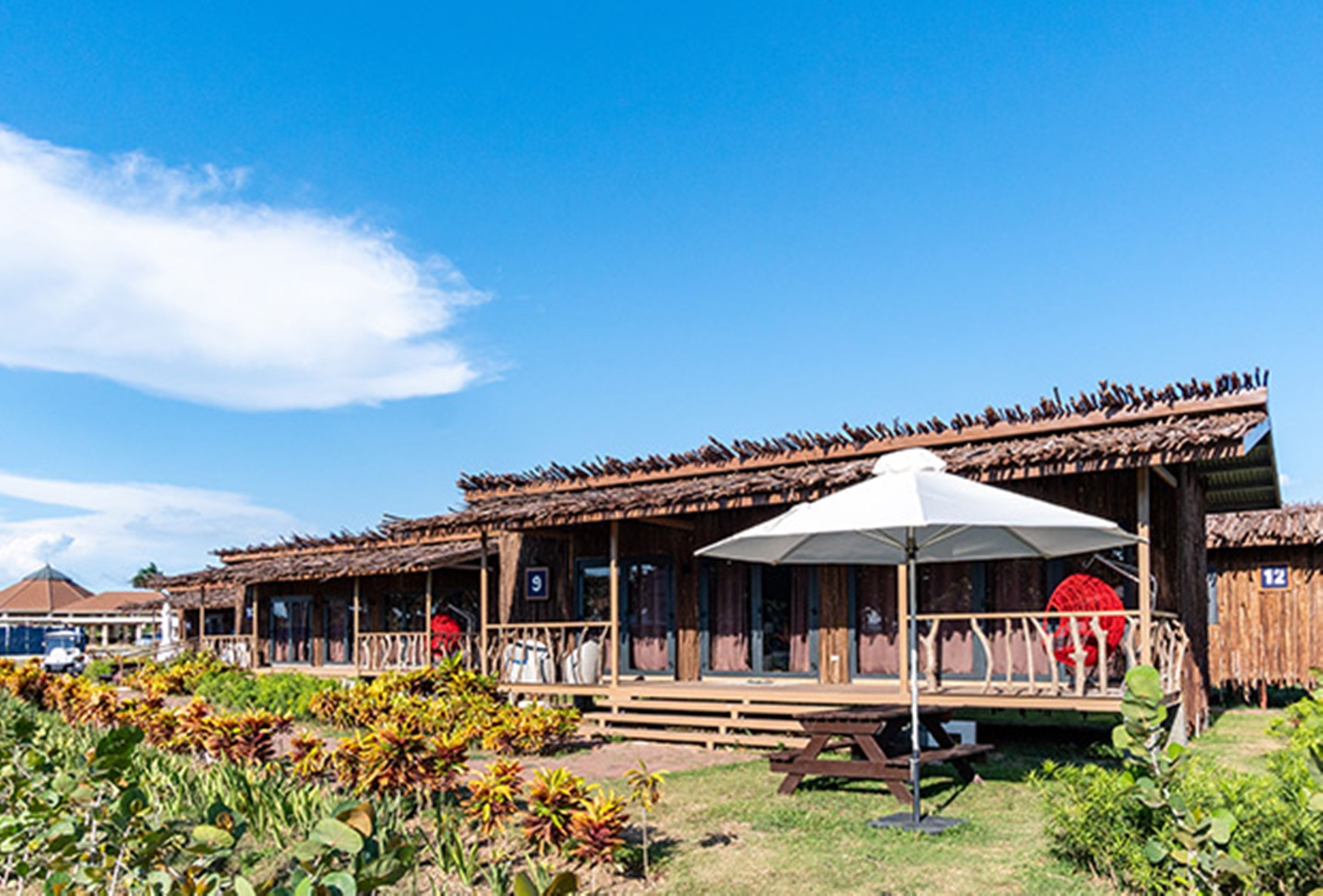 Un edificio rústico con techo de paja, un espacio al aire libre cubierto y una mesa de picnic.