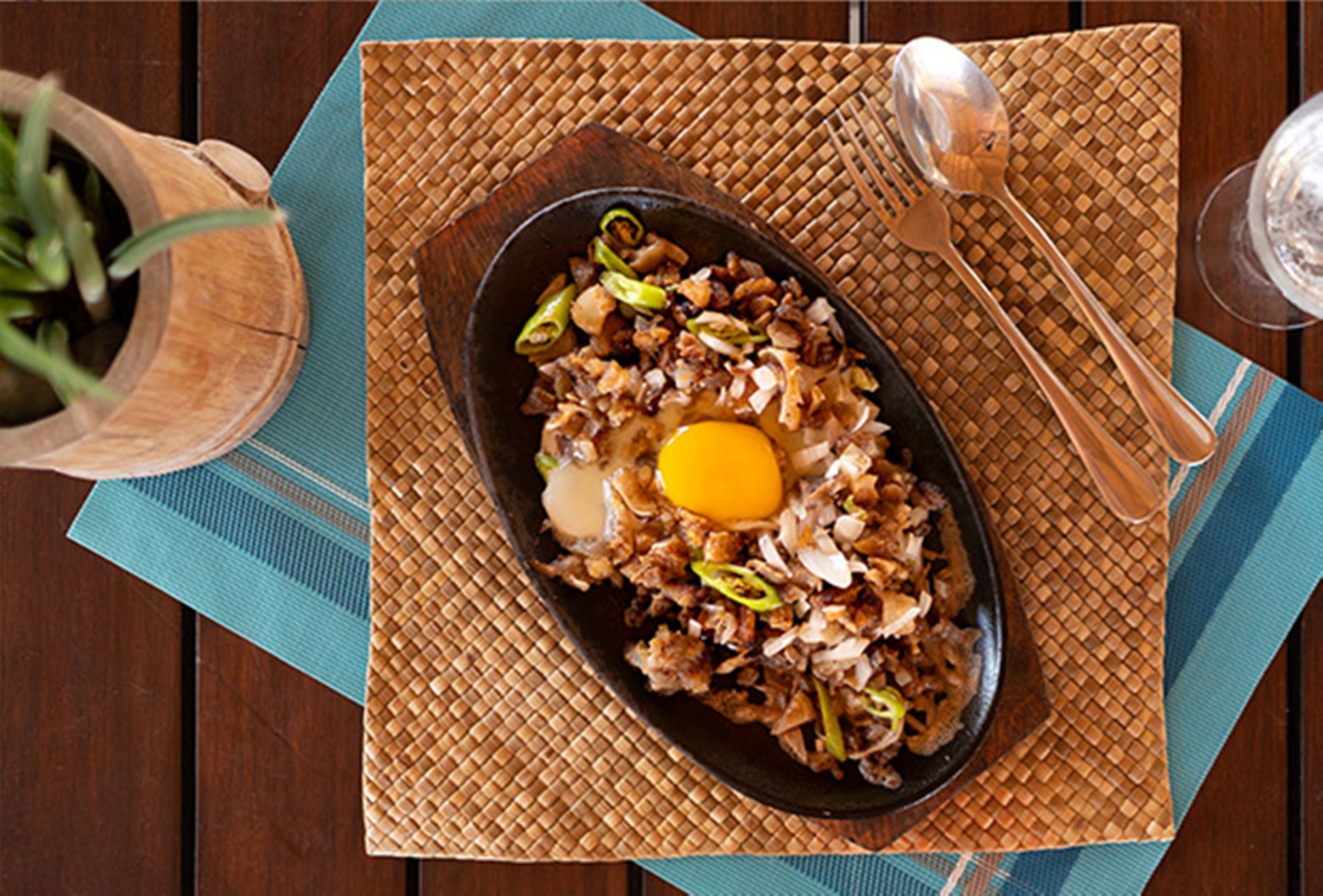 A dish with an egg on top, served on a black plate with a woven placemat underneath.