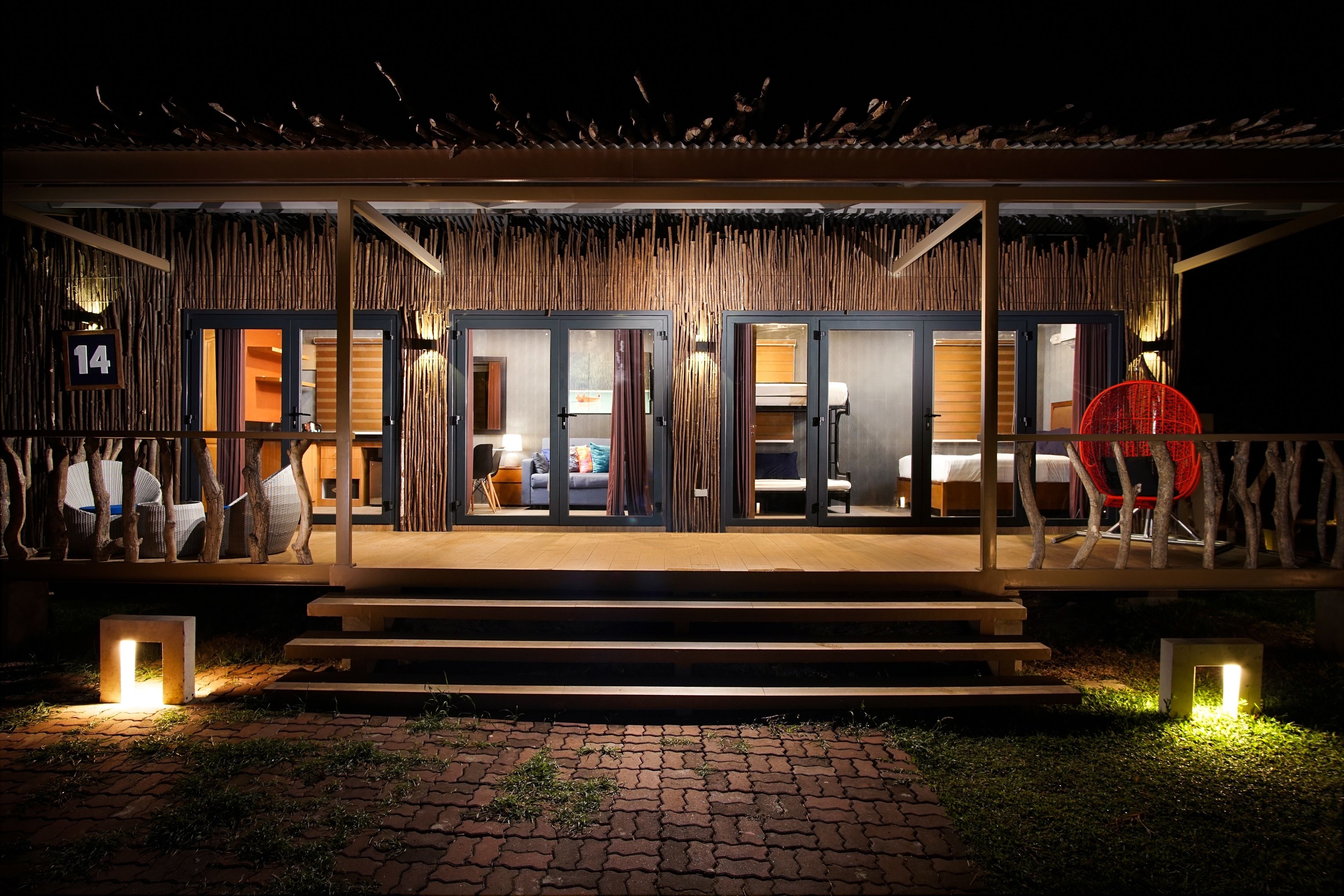A modern hotel with a thatched roof, wooden exterior, and a well-lit entrance.