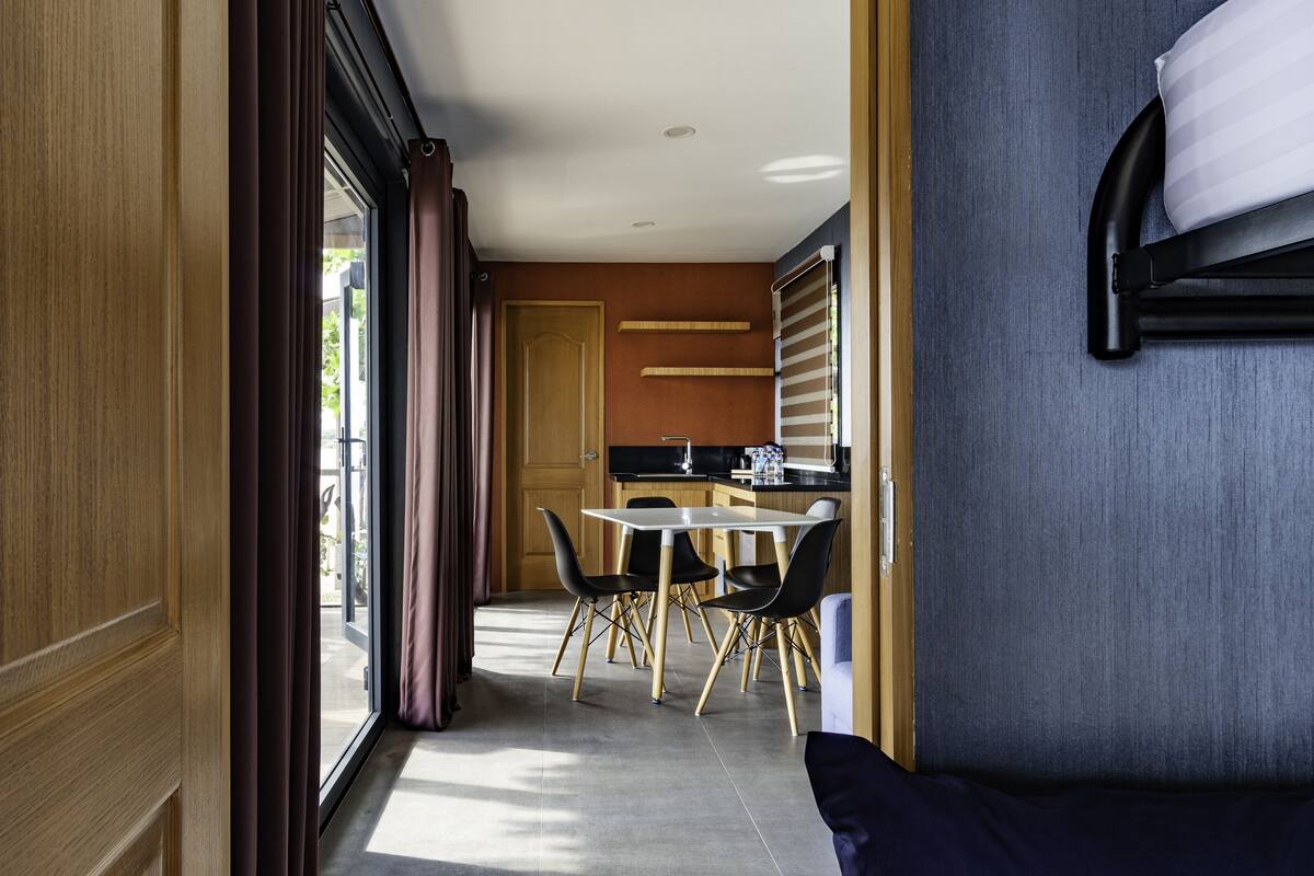 A modern hotel room with a dining area, a sofa, and a view through a large window.