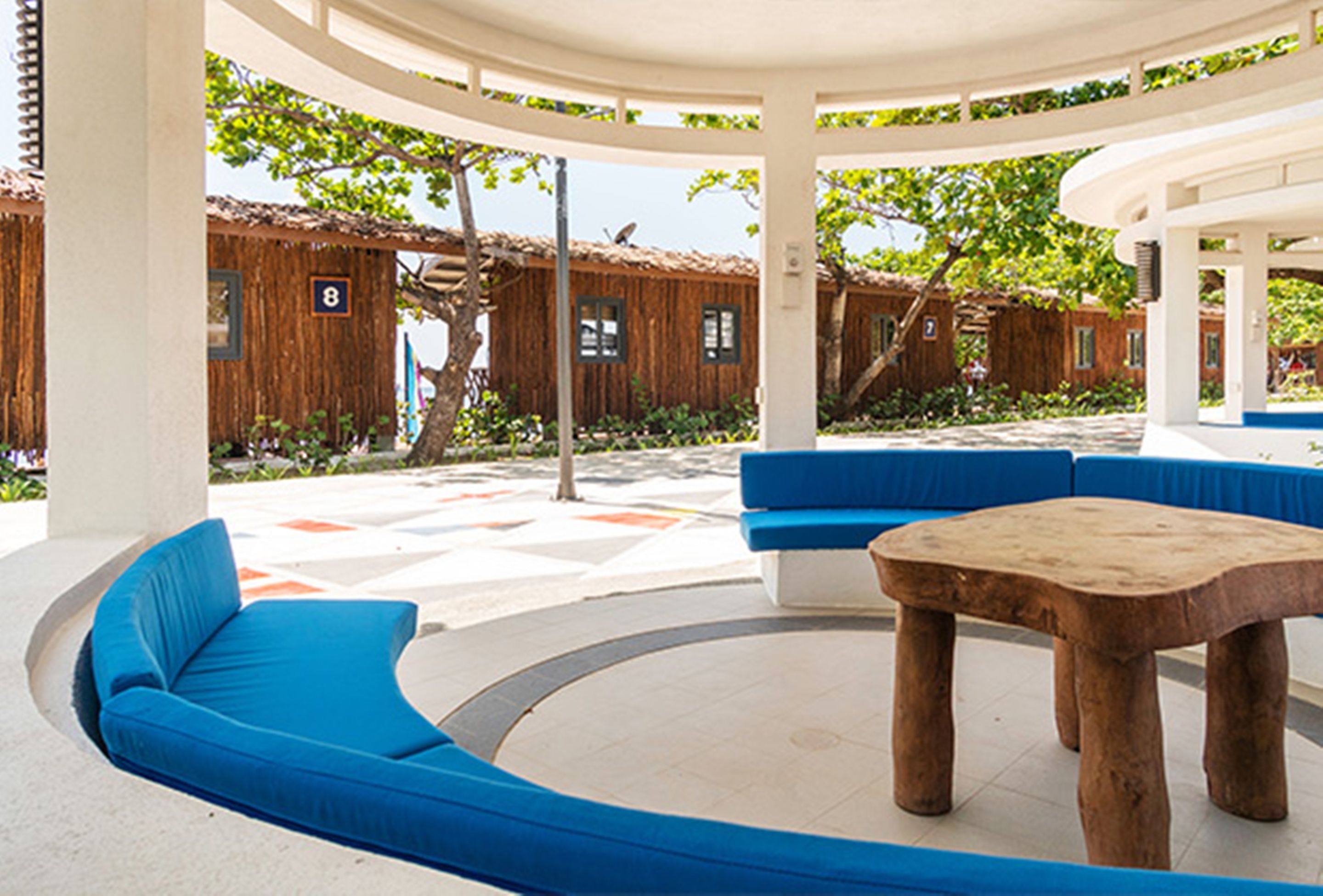 A covered outdoor seating area with blue cushioned benches and a wooden table.