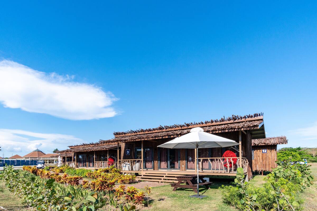 A rustic building with multiple rooms, a covered outdoor seating area, and a garden with various plants.