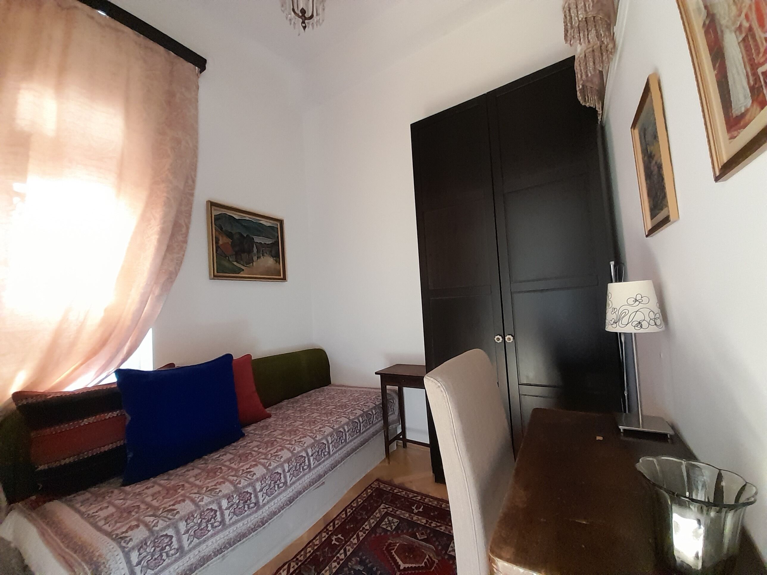 Une pièce avec un canapé à motifs, une porte sombre, une petite table, une lampe et une poubelle.