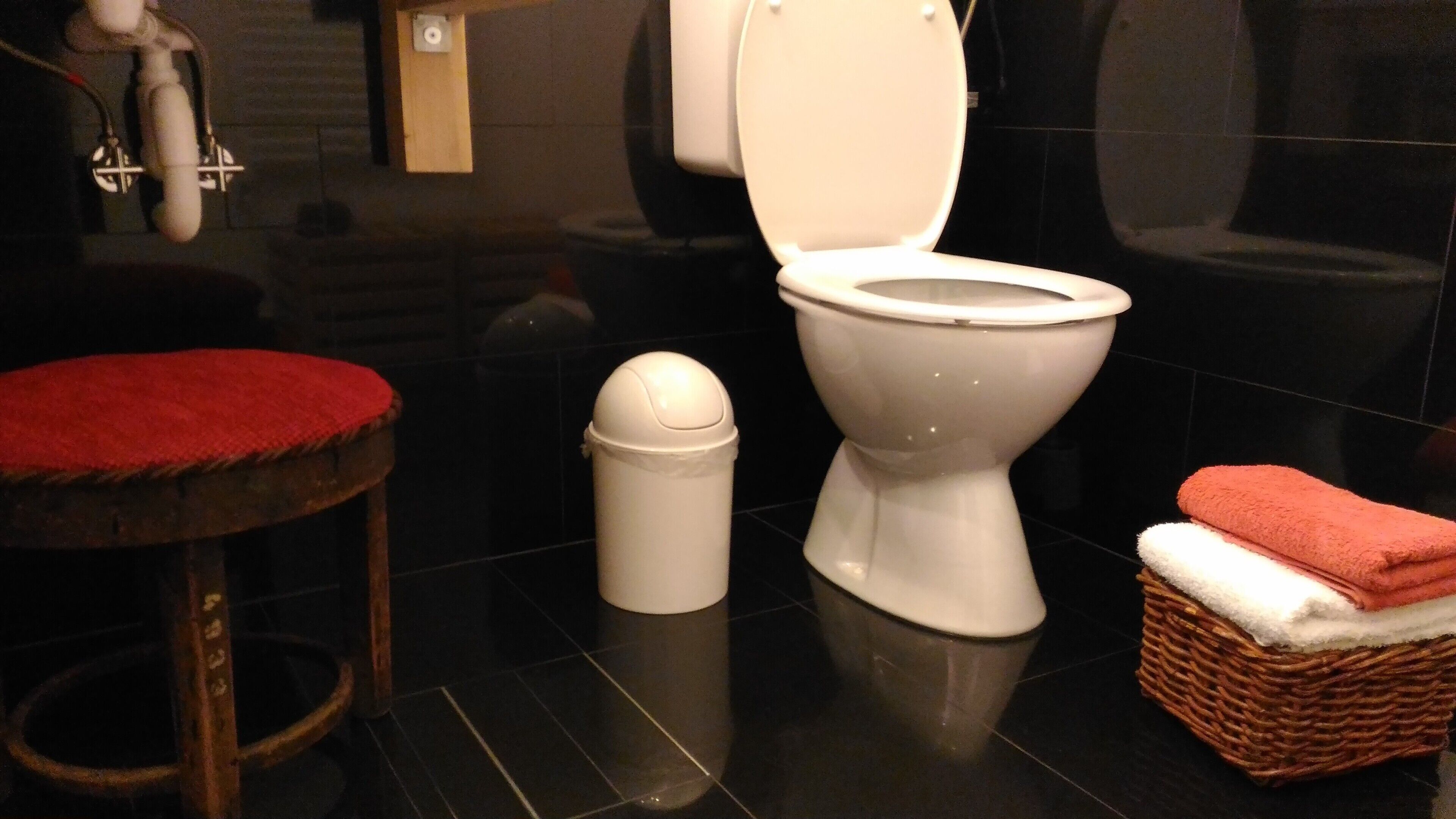 A modern bathroom with a white toilet, a trash bin, a red stool, and a wicker basket with towels.