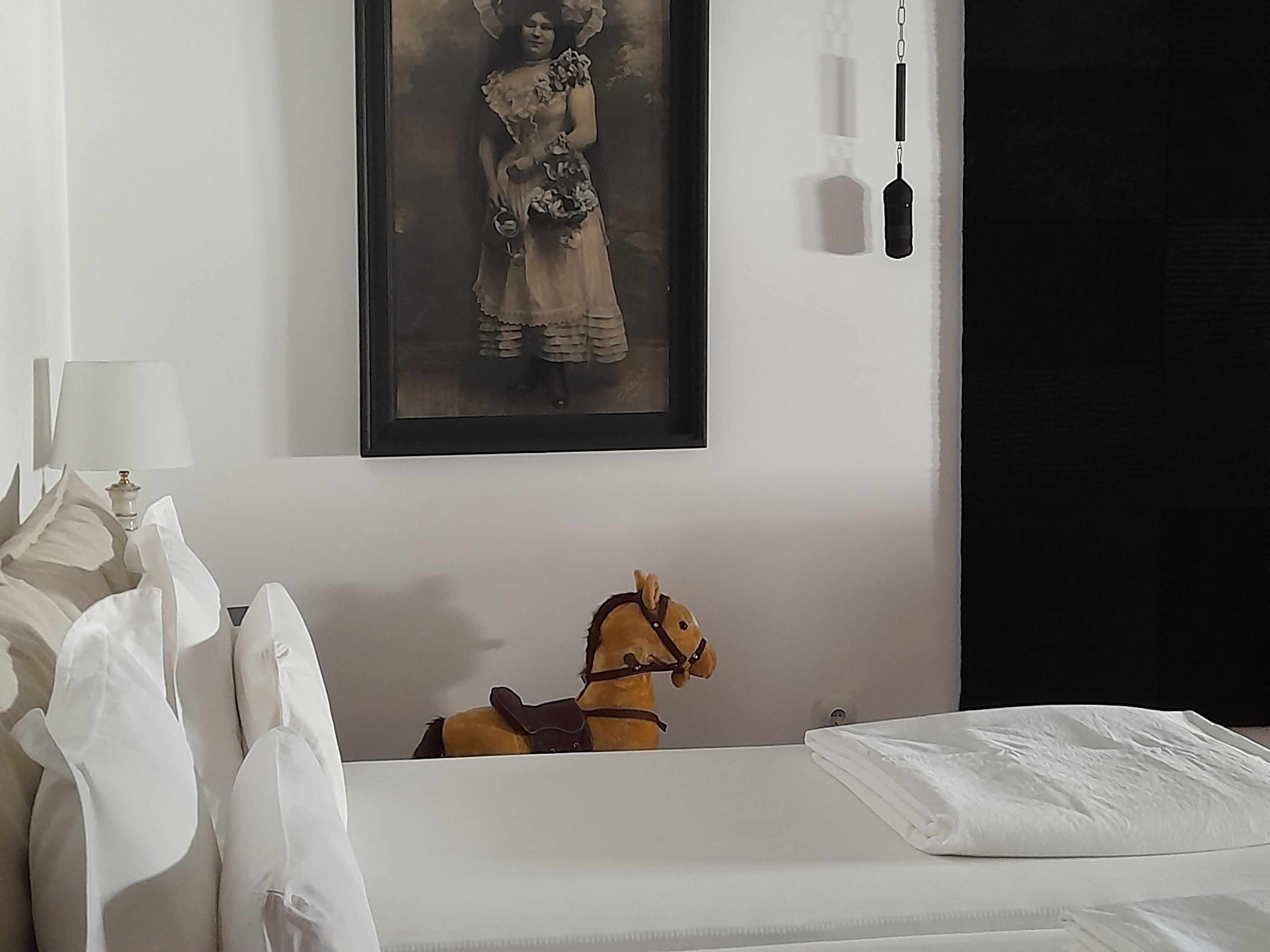 Een slaapkamer met een bed, een ingelijste foto aan de muur, een lamp en een speelgoedpaard.