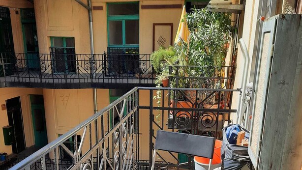 Un pequeño balcón exterior con una mesa dispuesta para dos, una planta en maceta y una silla.