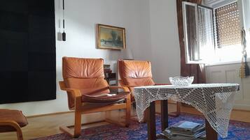 A room with two brown leather chairs, a wooden table with a white lace tablecloth, a patterned rug, and a painting on the wall.