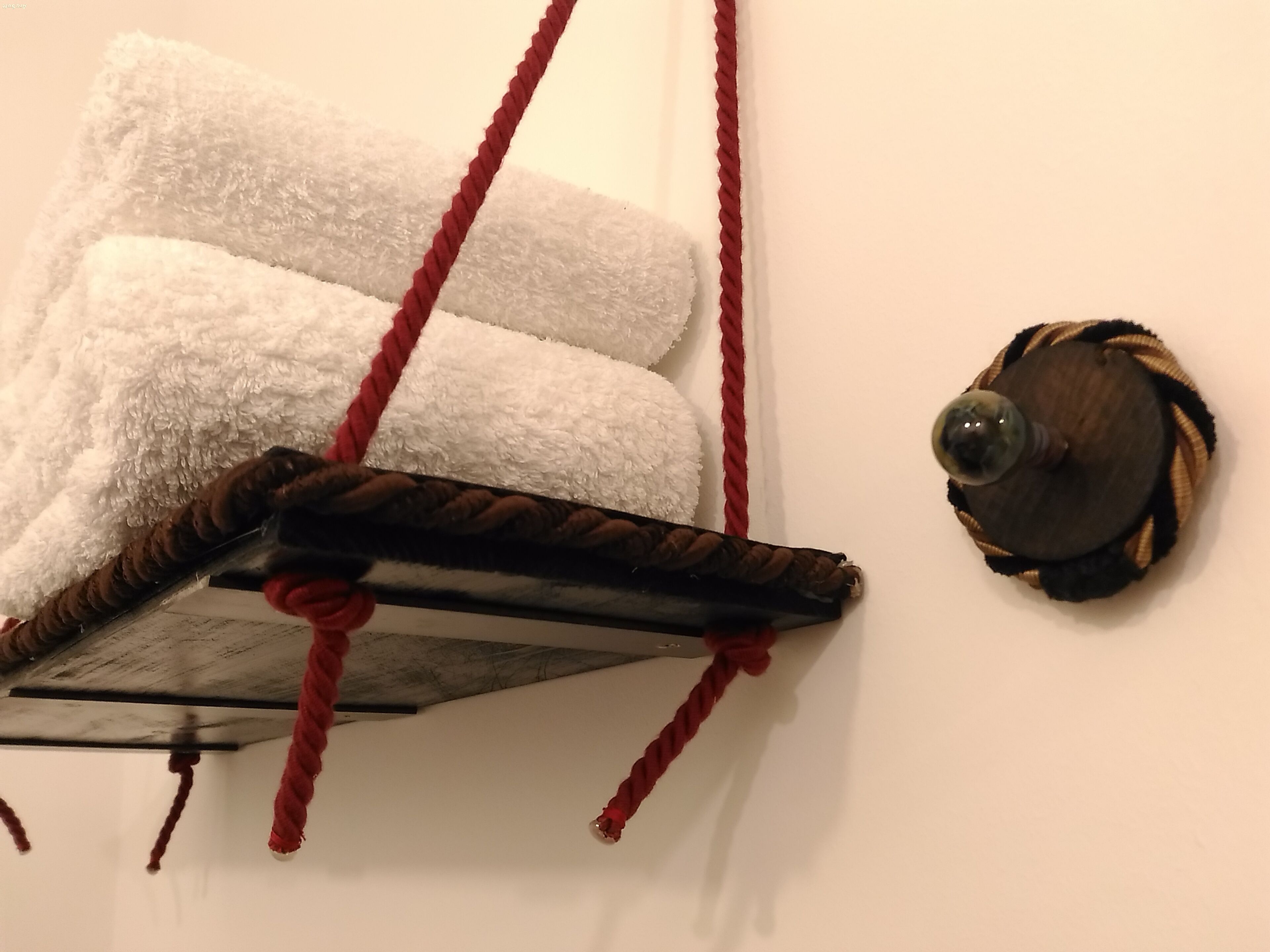 Un arbre à chat avec une base en bois et des cordes rouges, fixé à un mur blanc.