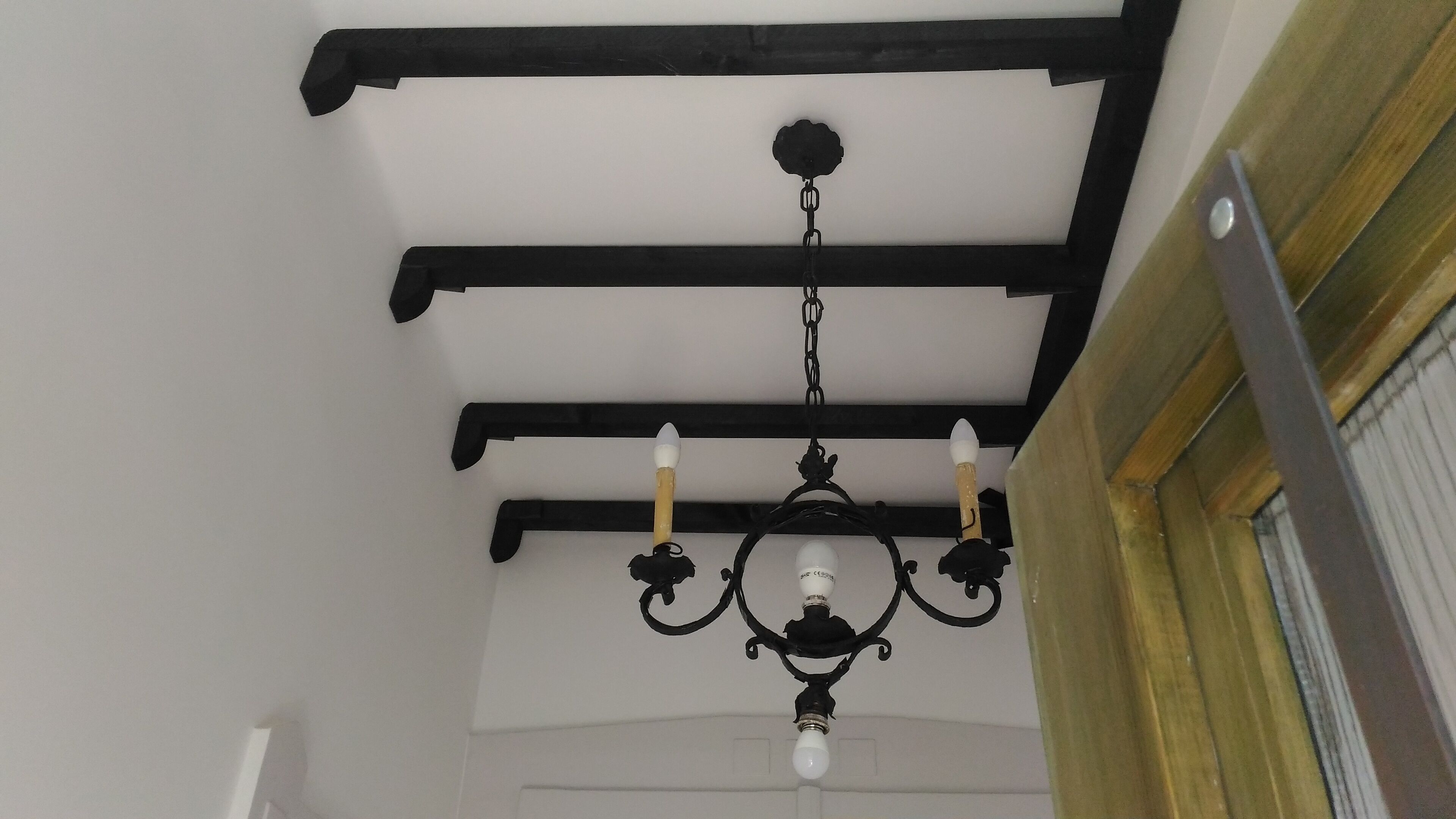 A chandelier with four candle-like lights hanging from a black metal frame.