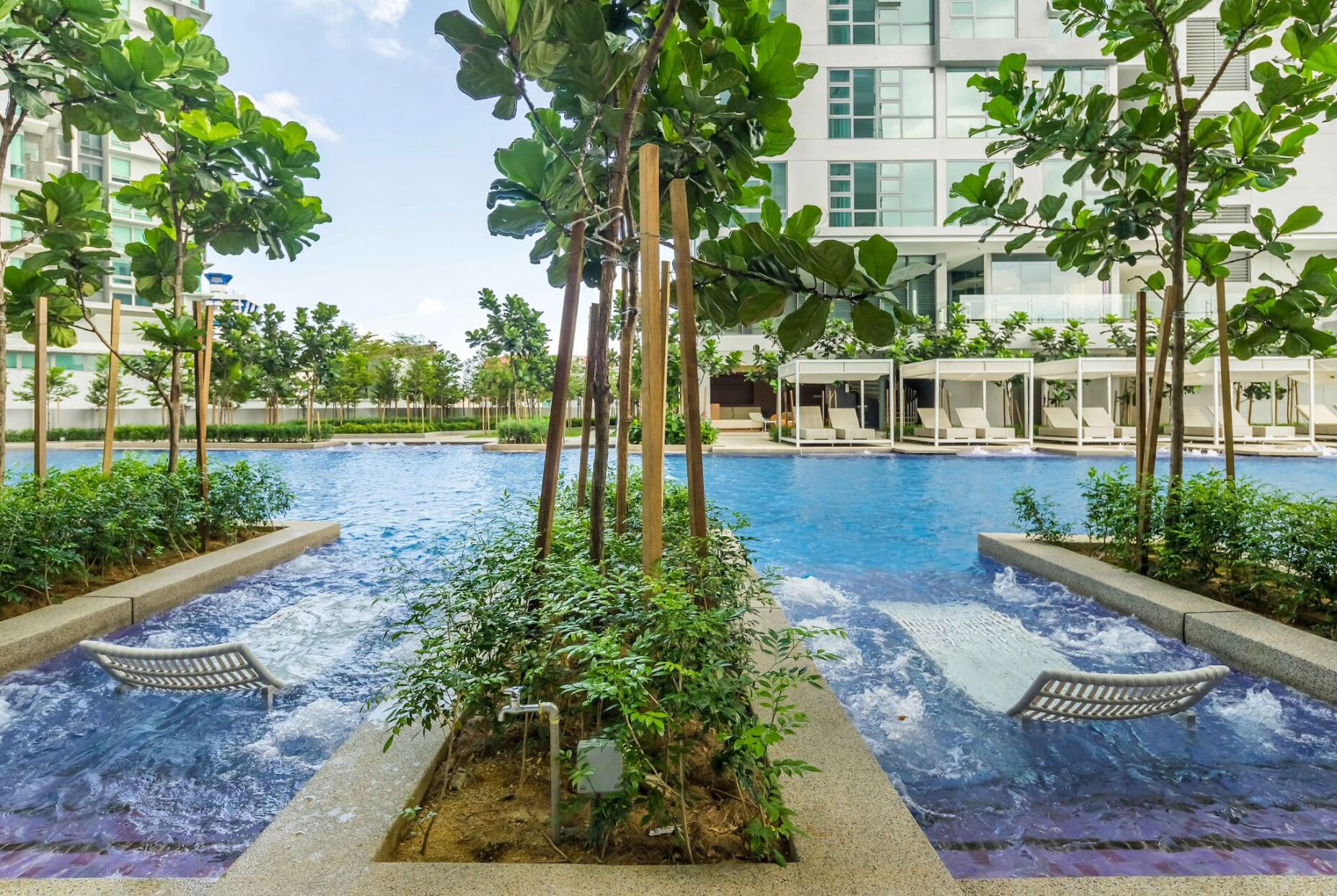 A swimming pool with a waterfall feature surrounded by greenery and lounge chairs.