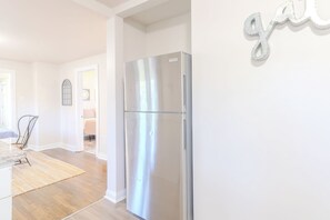 Una cocina moderna con un refrigerador de acero inoxidable, un comedor con encimera de mármol y vistas a un dormitorio a través de una puerta abierta.