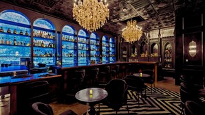 Un espace bar doté de plusieurs étagères remplies de bouteilles d’alcool, d’un lustre et d’un sol à motifs.