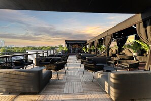 Une terrasse avec des sièges extérieurs et une vue sur les gratte-ciel de la ville au coucher du soleil.