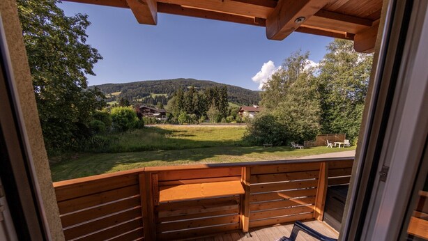 A wooden deck with a bench and two chairs, overlooking a grassy area with trees and a distant mountain. - Family & Freelance Apartment in the center of Ski Amadé (Altenmarkt im Pongau)