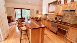 Una cocina moderna con armarios de madera, una isla central, taburetes de bar y un comedor con sillas.