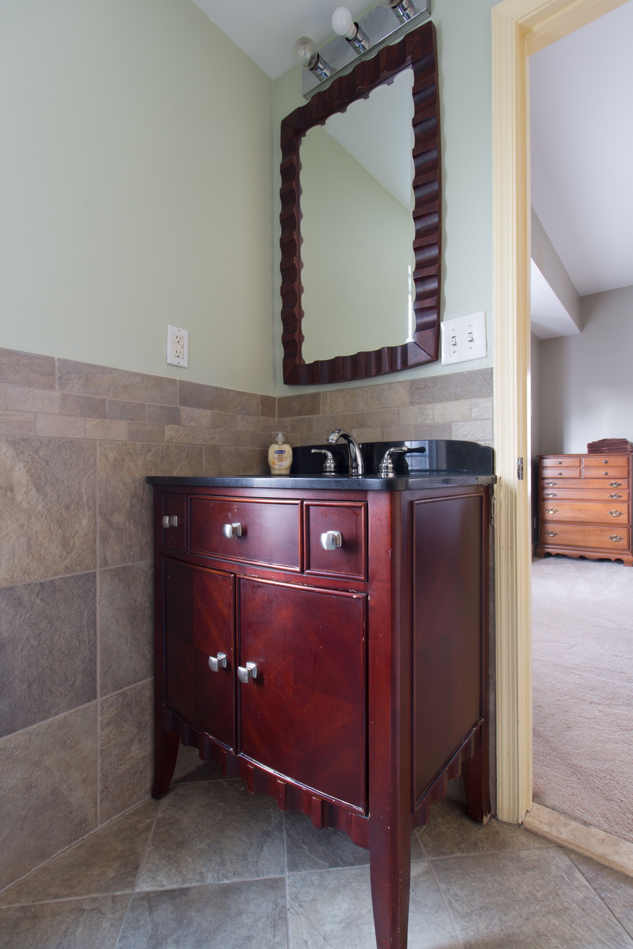 A bathroom with a wooden vanity, a mirror, and a tiled floor.