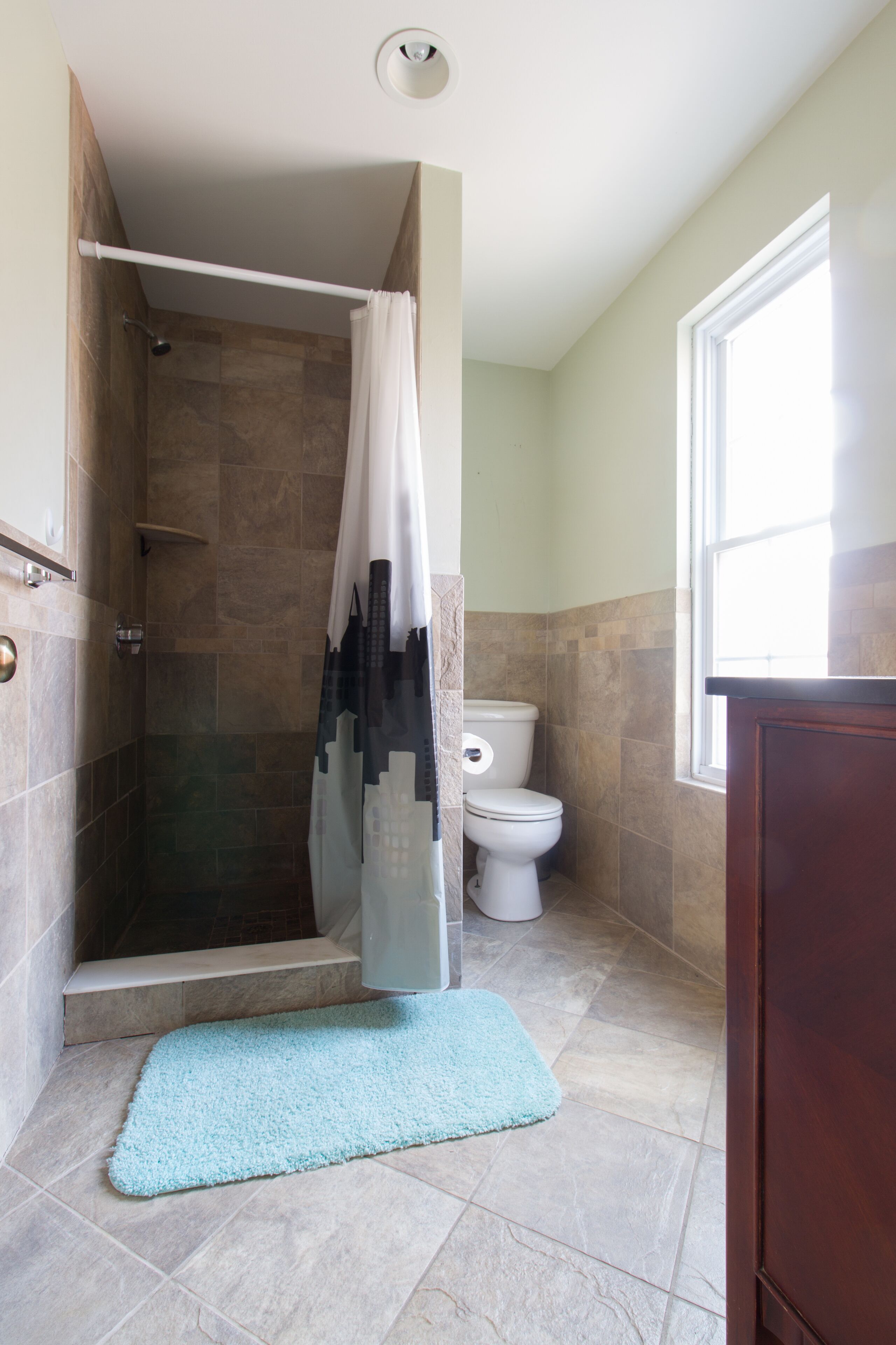 A bathroom with a shower, toilet, and a window.