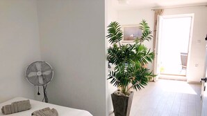 Una habitación de hotel con una cama, un ventilador de pie, una planta en maceta y vistas al exterior.